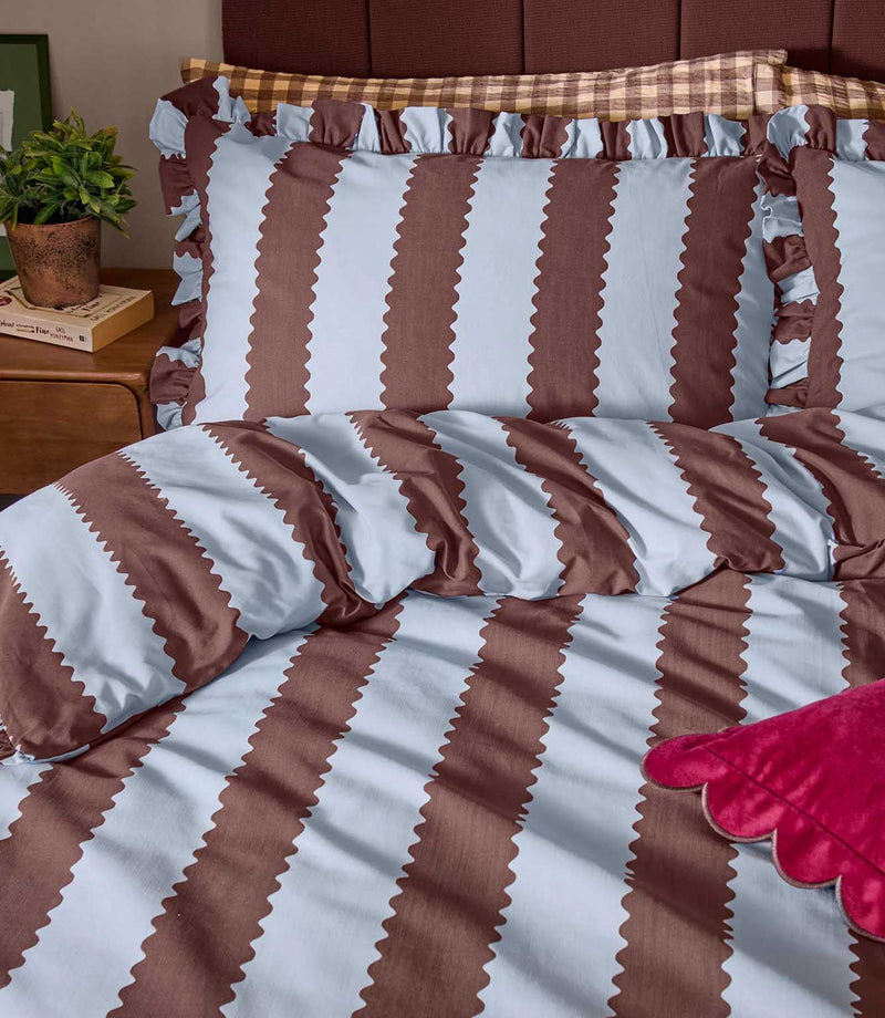 Close-up of the Birdie Stripe Ruffle bedding in chocolate brown and pale blue, showing the scalloped stripe design, soft fabric texture and gathered ruffle trim on the pillowcases.