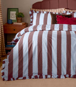Birdie Stripe Ruffle duvet cover set in chocolate brown and pale blue, styled on a bed with matching striped pillowcases, ruffled edges and layered decorative cushions.
