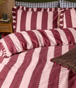 Close-up of the Birdie Stripe Ruffle bedding in burgundy and blush pink, showing the scalloped stripe pattern, soft fabric texture and gathered ruffle trim on the matching pillowcases.