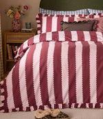 Birdie Stripe Ruffle duvet cover set in burgundy and blush pink, styled with matching striped pillowcases, ruffled edges and layered decorative cushions in a cosy bedroom setting.