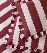 Detailed close-up of the Birdie Stripe Ruffle pillowcase and duvet cover in burgundy and blush pink, highlighting the scalloped stripe design, woven-look texture and gathered two-tone ruffle trim.