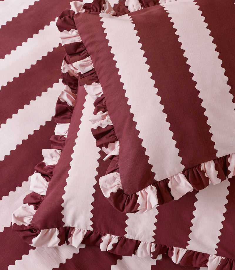 Detailed close-up of the Birdie Stripe Ruffle pillowcase and duvet cover in burgundy and blush pink, highlighting the scalloped stripe design, woven-look texture and gathered two-tone ruffle trim.