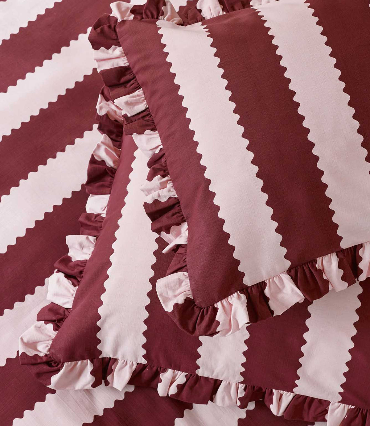 Detailed close-up of the Birdie Stripe Ruffle pillowcase and duvet cover in burgundy and blush pink, highlighting the scalloped stripe design, woven-look texture and gathered two-tone ruffle trim.
