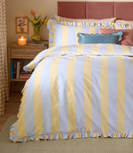 Birdie Stripe Ruffle duvet cover set in lemon yellow and sky blue, styled on a bed with matching striped ruffle pillowcases, decorative cushions and soft bedroom accessories.