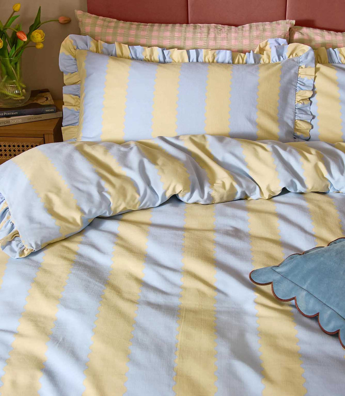 Close-up of Birdie Stripe Ruffle bedding in lemon yellow and sky blue, showing the scalloped stripe pattern, soft fabric texture and gathered two-tone ruffle trim on the pillowcases.
