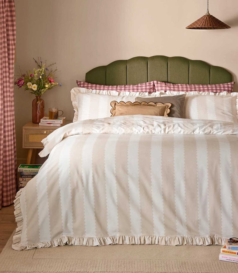 Birdie Stripe Ruffle duvet cover set in oat beige and soft white, featuring subtle scalloped vertical stripes and gathered ruffle edging, styled with matching pillowcases and layered cushions.