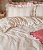 Close-up of the Birdie Stripe Ruffle bedding in oat beige and soft white, showing the tonal scalloped stripe design, soft woven-look texture and gathered ruffle trim on the pillowcases.