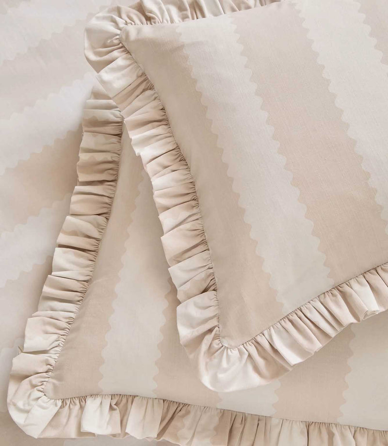 Detailed close-up of the Birdie Stripe Ruffle duvet cover and pillowcase in oat beige and soft white, highlighting the subtle scalloped stripe pattern, fabric texture and gathered ruffle edging.