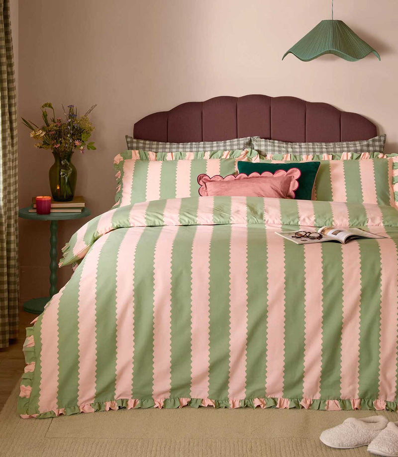 Birdie Stripe pink and green duvet cover set with scalloped vertical stripes and ruffled edging, styled with coordinating cushions in a colourful bedroom.