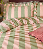 Close-up of Birdie Stripe pink and green bedding, showing scalloped striped pillowcases with ruffled edges, matching duvet cover and pink velvet cushion.