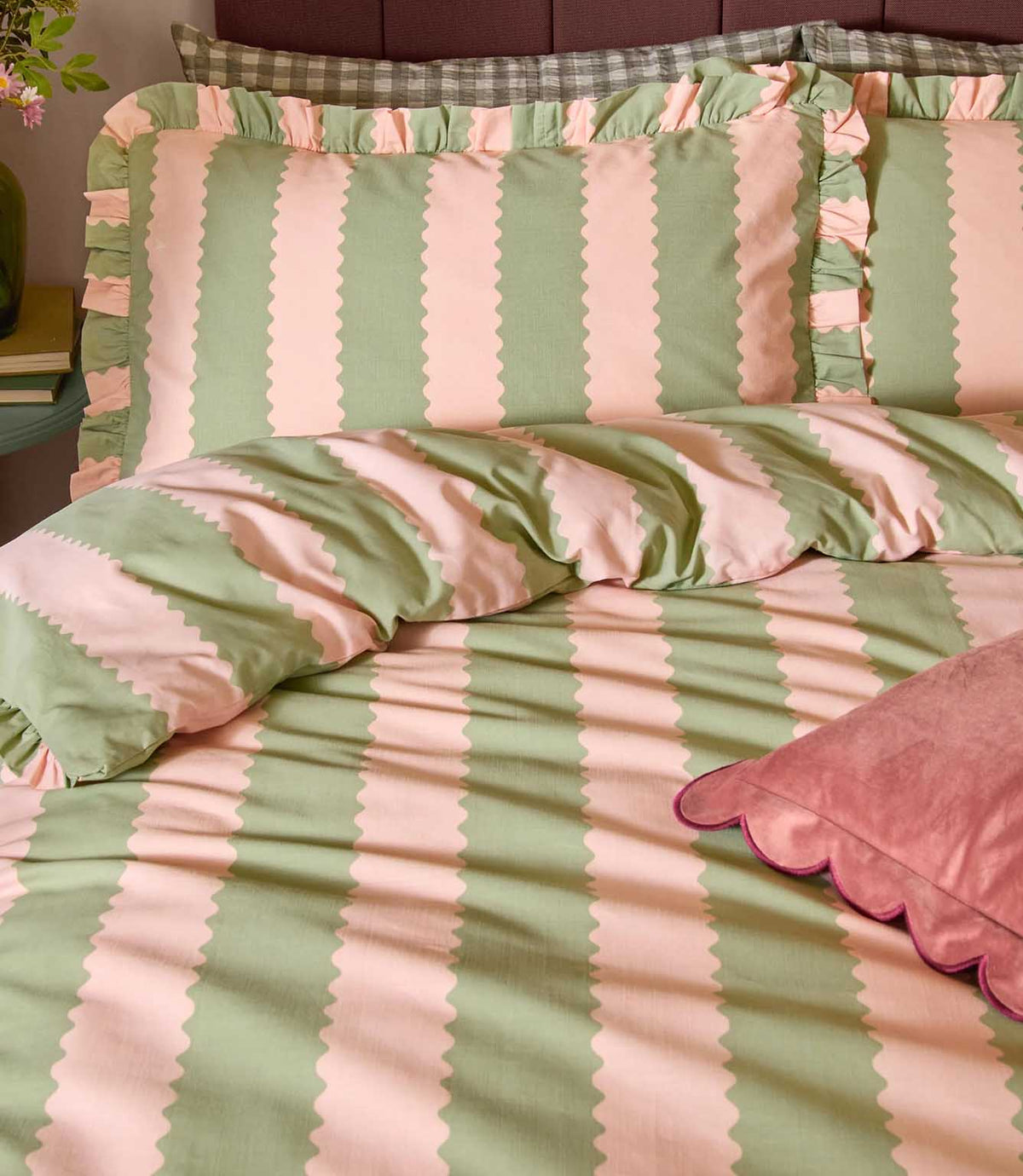 Close-up of Birdie Stripe pink and green bedding, showing scalloped striped pillowcases with ruffled edges, matching duvet cover and pink velvet cushion.