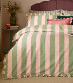 Birdie Stripe pink and green striped duvet cover and matching ruffled pillowcases, styled on a bed with decorative cushions and bedside flowers.