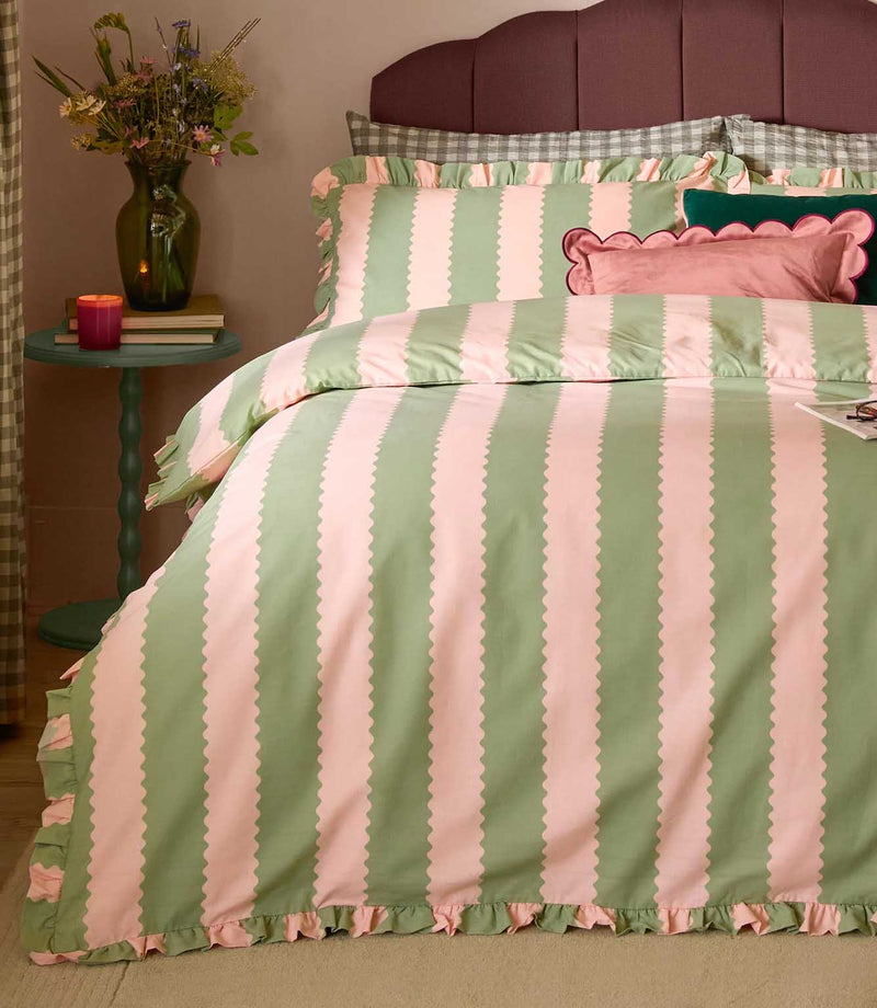 Birdie Stripe pink and green striped duvet cover and matching ruffled pillowcases, styled on a bed with decorative cushions and bedside flowers.