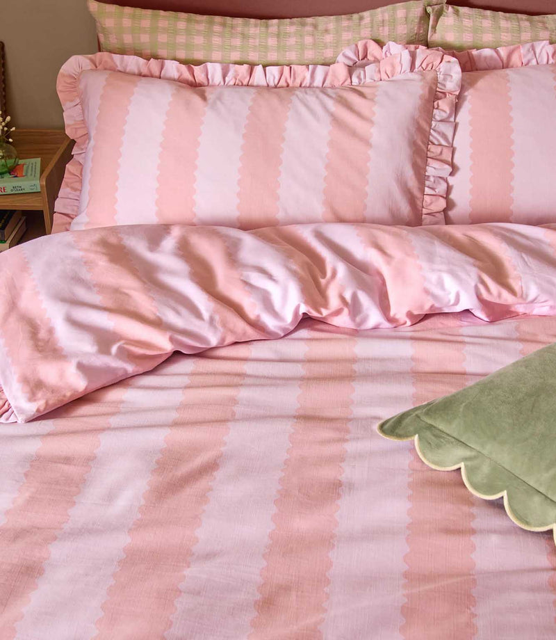 Close-up of Birdie Stripe pink and raspberry striped bedding, showing the ruffled pillowcases and matching duvet cover with soft scalloped stripe detailing.