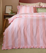 Birdie Stripe pink and raspberry duvet cover and matching ruffled pillowcases, styled with green and pink cushions against a curved upholstered headboard.