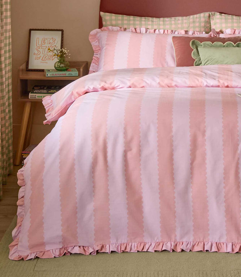Birdie Stripe pink and raspberry duvet cover and matching ruffled pillowcases, styled with green and pink cushions against a curved upholstered headboard.
