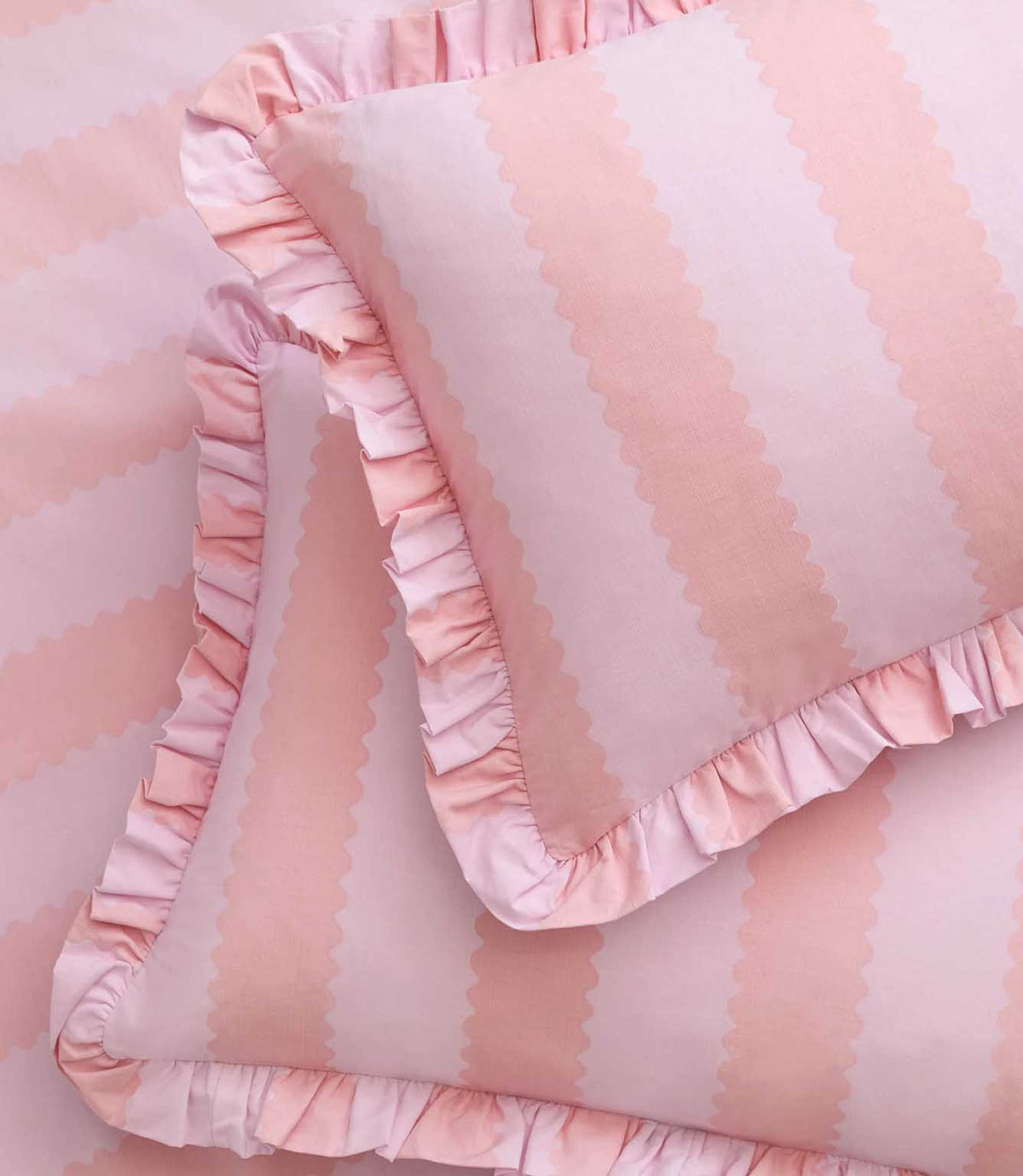 Detailed close-up of Birdie Stripe pink and raspberry pillowcases, featuring scalloped vertical stripes and decorative pink ruffle edging on matching bedding.