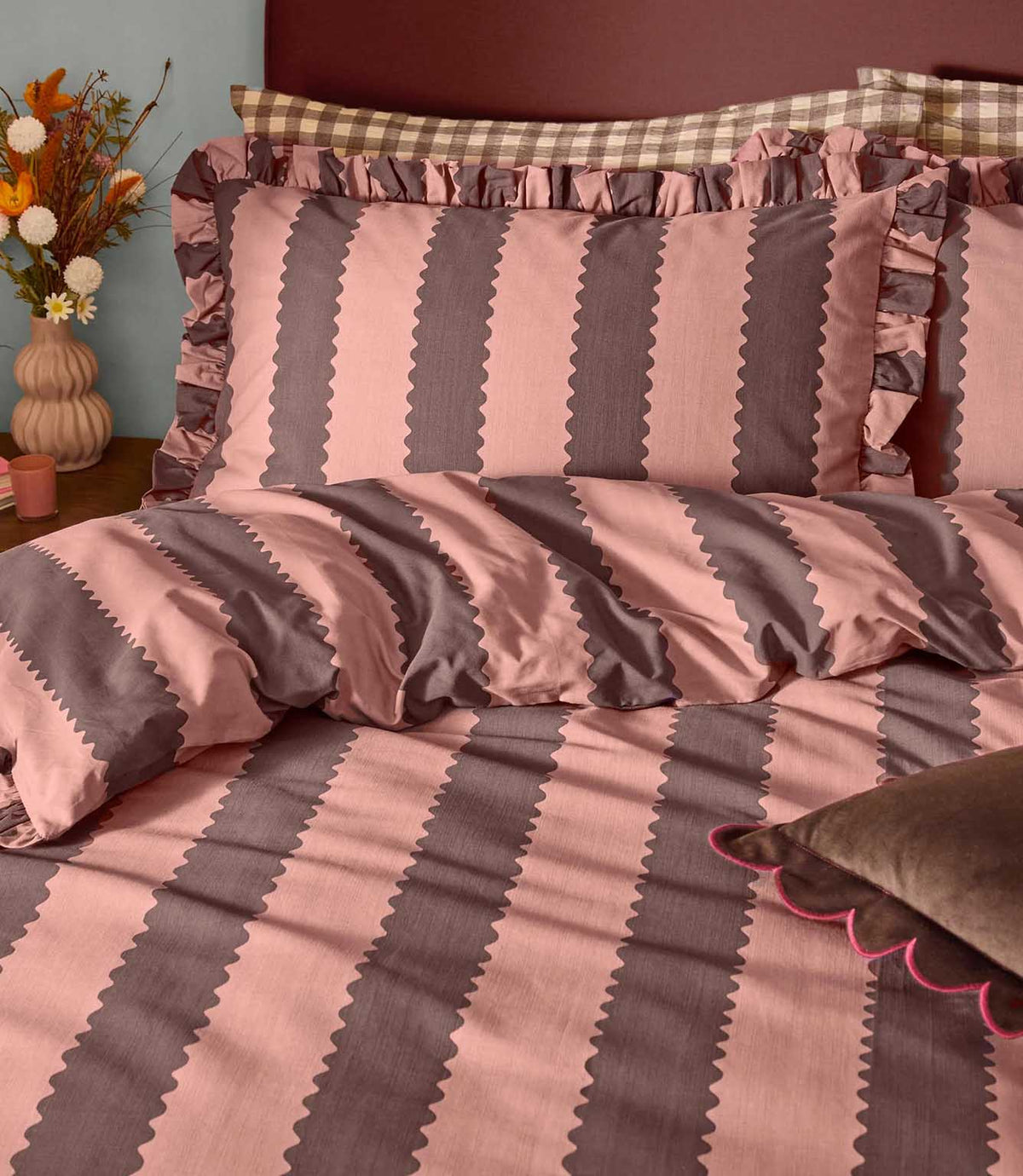 Close-up of Birdie Stripe rose and chocolate bedding, showing scalloped striped pillowcases with ruffled edges and a matching striped duvet cover.