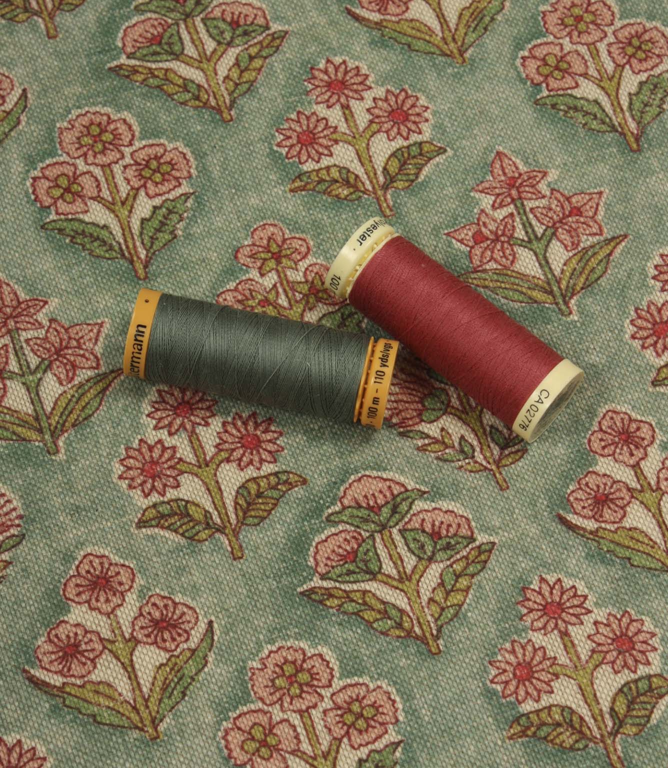 Floral patterned fabric with pink and green thread spools displayed for colour matching inspiration.