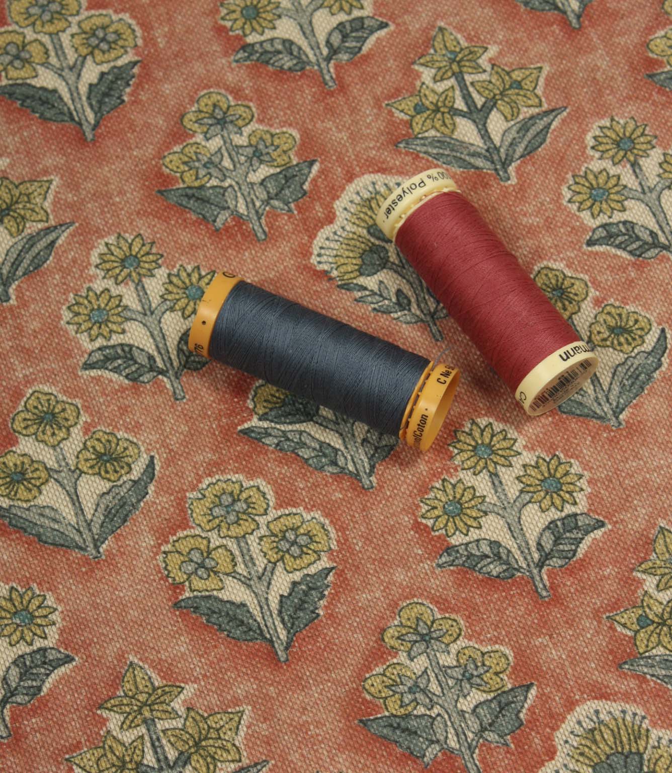 Boho Blossom floral fabric with coordinating navy and coral thread spools displayed on the terracotta ditsy floral pattern.