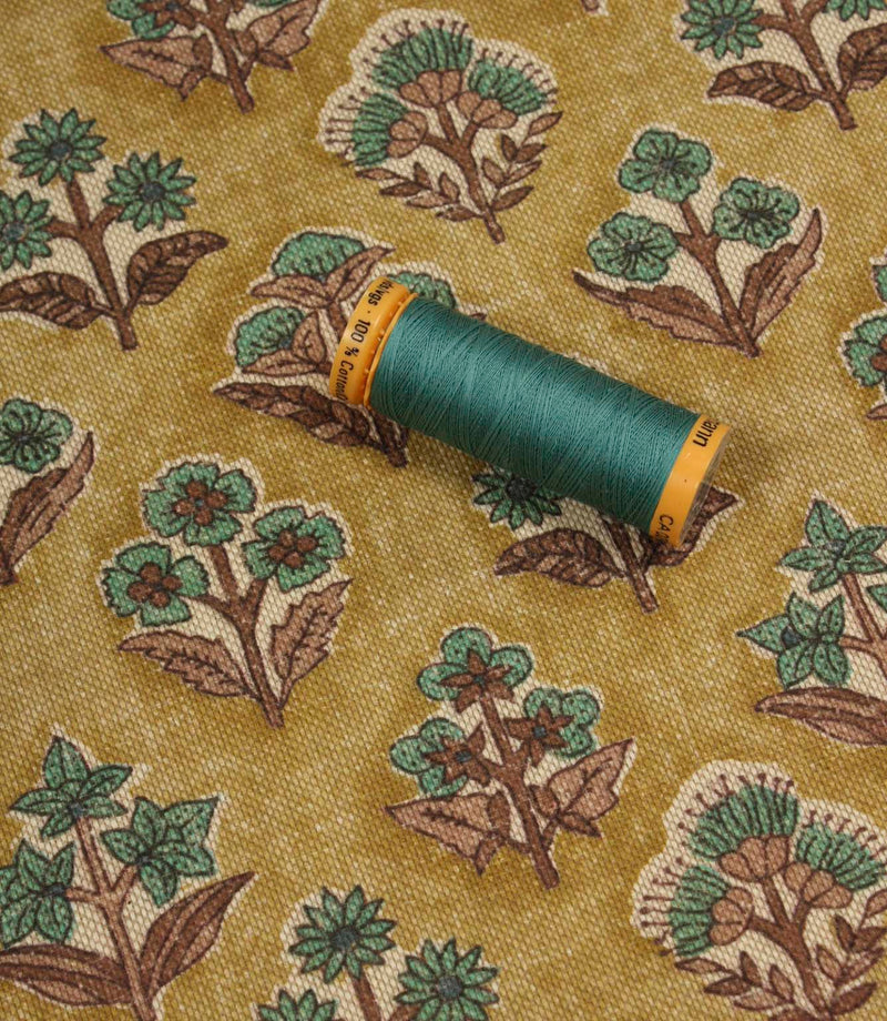 Boho Blossom floral fabric with coordinating teal thread spool displayed on the patterned mustard yellow fabric.