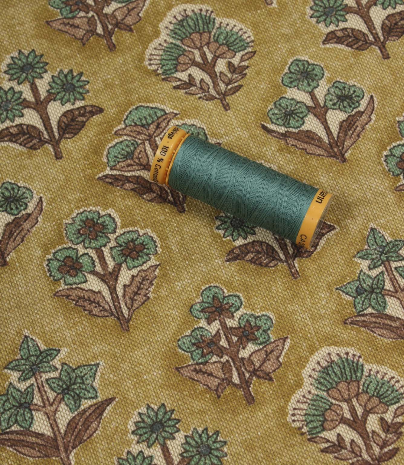 Boho Blossom floral fabric with coordinating teal thread spool displayed on the patterned mustard yellow fabric.