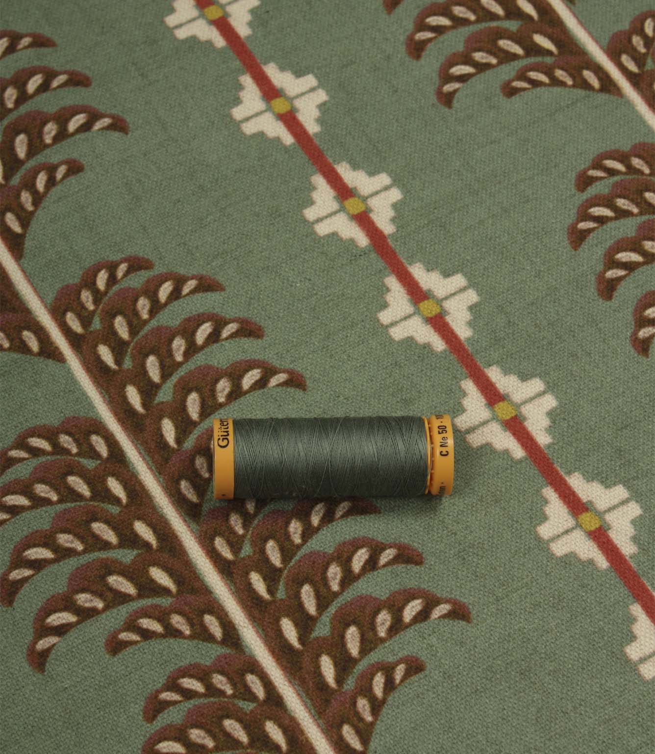 Boho Trail Mineral upholstery and curtain fabric displayed with coordinating green thread, highlighting the botanical motif and heritage-inspired design.