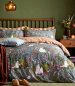 Bootanical Forest reversible Halloween duvet cover set on a wooden bed, featuring white ghosts among pink, orange, purple and white wildflowers on a soft blue-grey ground, with a rust and cream striped reverse.