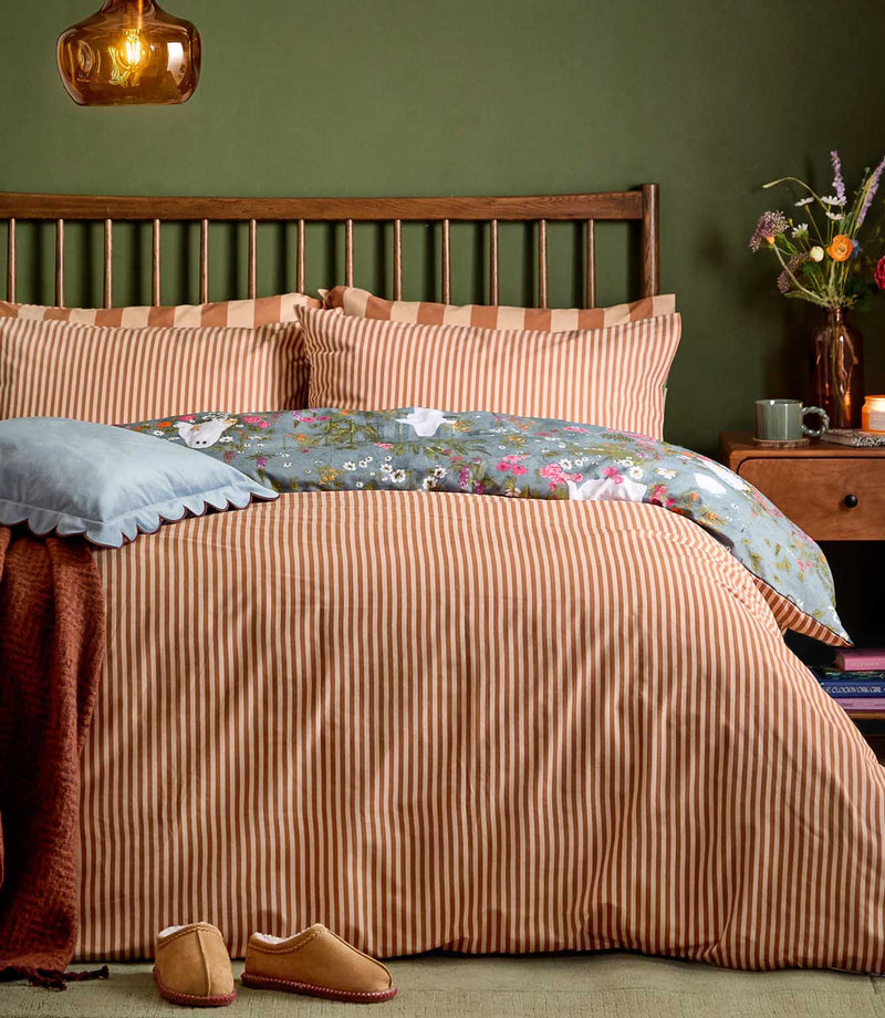 Bootanical Forest duvet cover displayed on its rust and cream striped reverse, with the blue-grey ghost and colourful wildflower print folded back across the top of the bed.