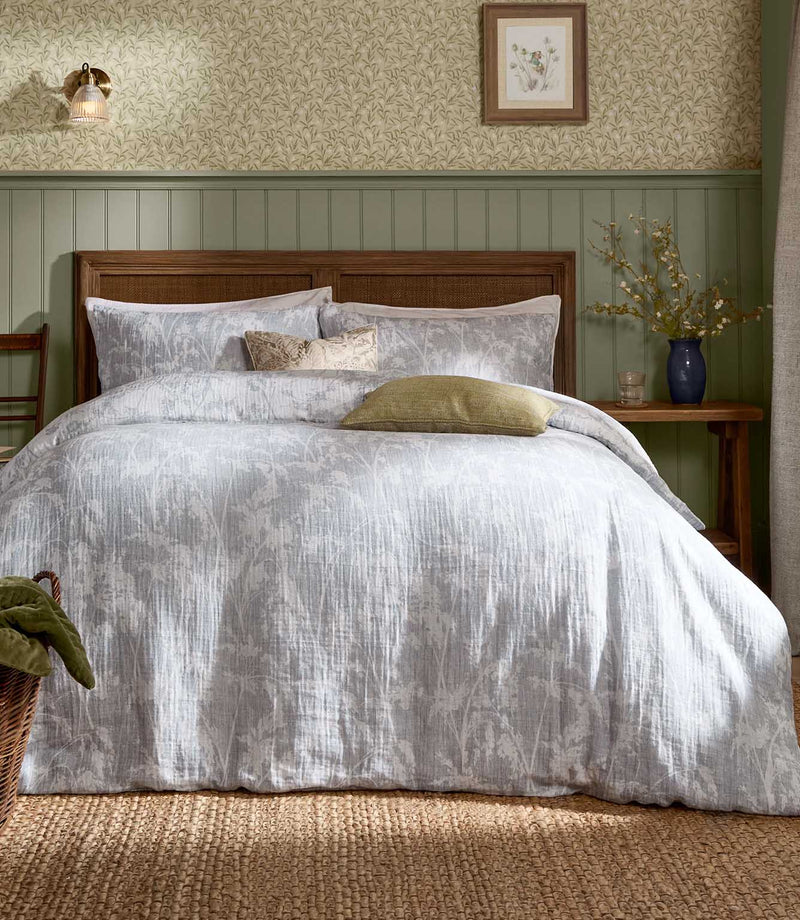 Voyage Maison Braeflower Reversible Muslin Duvet Cover Set in a soft grey colourway, styled on a wooden bed in a country-inspired bedroom.