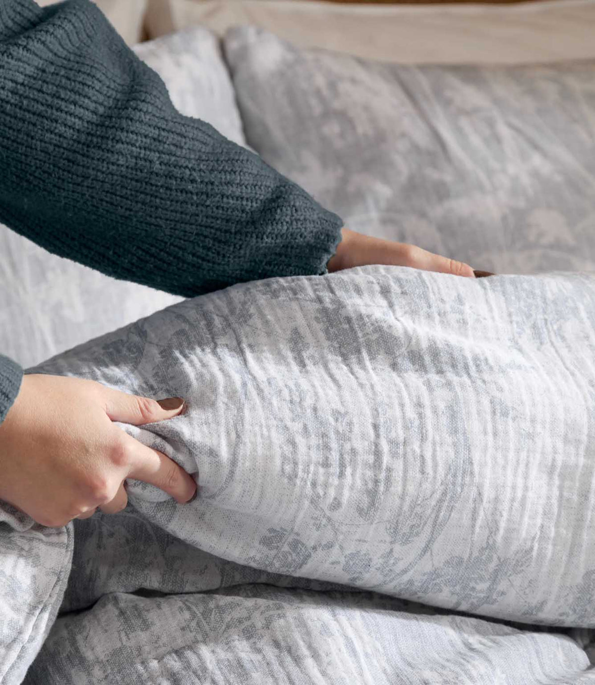 Hands arranging the Voyage Maison Braeflower muslin duvet cover in soft grey, highlighting the lightweight textured fabric and subtle botanical print.