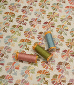 Briar Sprig Jasmine washable woven upholstery fabric displayed with coordinating pink, green and blue threads on a cream ground with colourful floral sprigs.