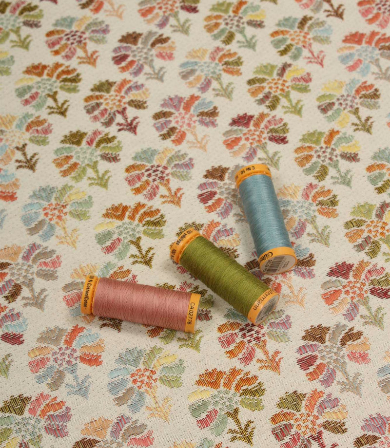 Briar Sprig Jasmine washable woven upholstery fabric displayed with coordinating pink, green and blue threads on a cream ground with colourful floral sprigs.