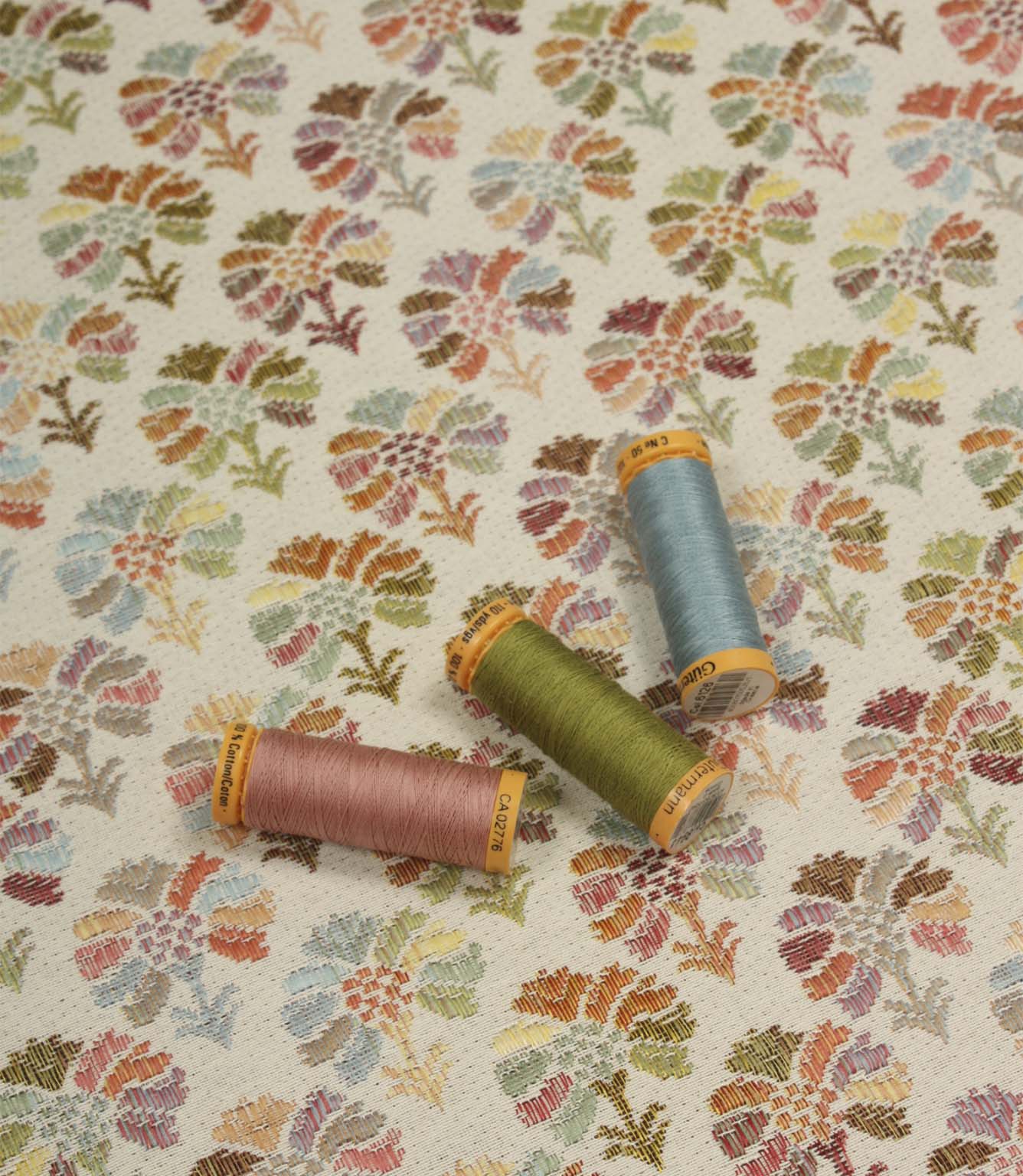 Briar Sprig Jasmine washable woven upholstery fabric displayed with coordinating pink, green and blue threads on a cream ground with colourful floral sprigs.
