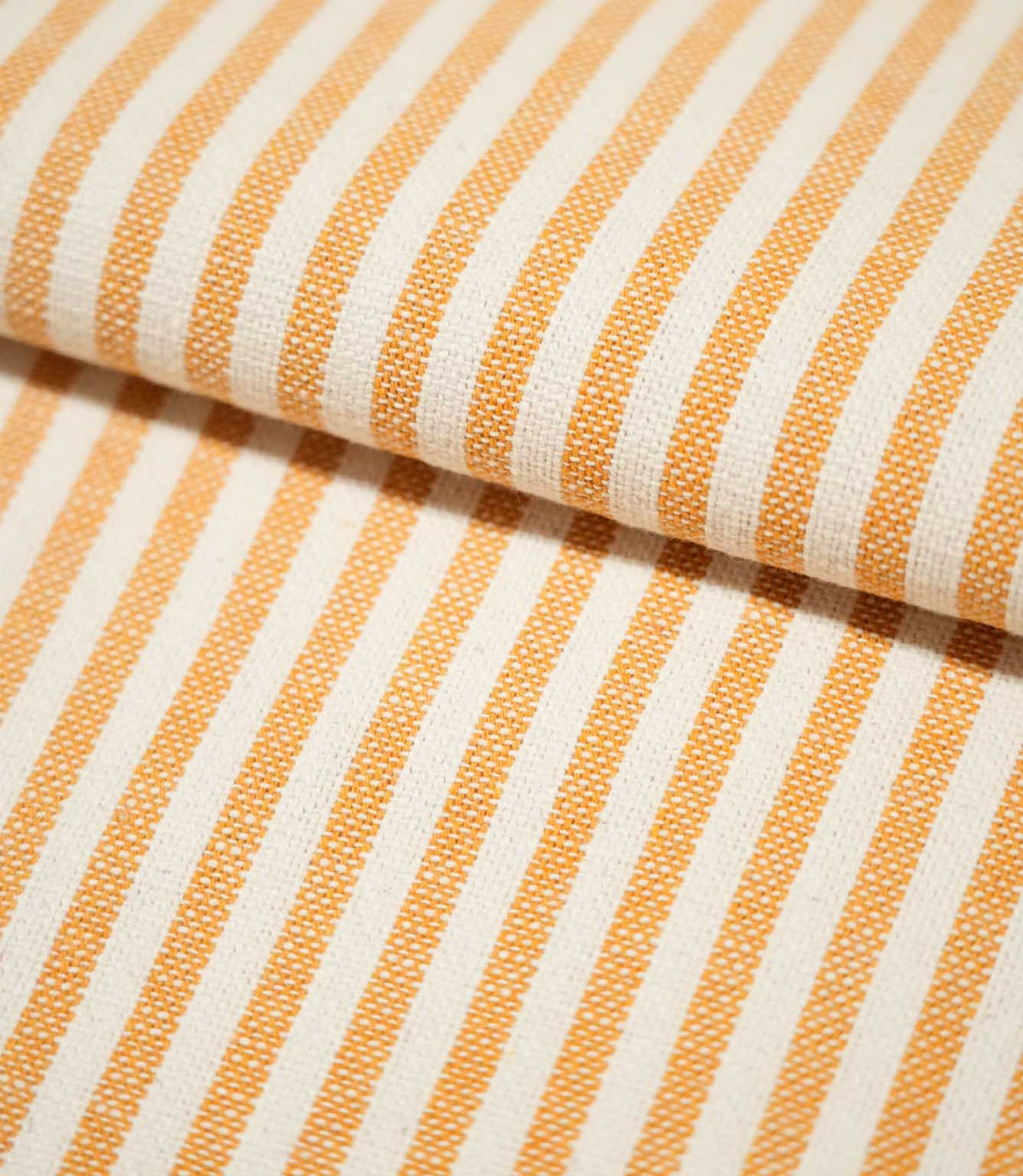 Close-up of Broadway Stripe Sunflower fabric folded over itself, highlighting the crisp alternating orange and off-white stripes, consistent stripe spacing and tactile woven surface as the pattern curves naturally around the fold.