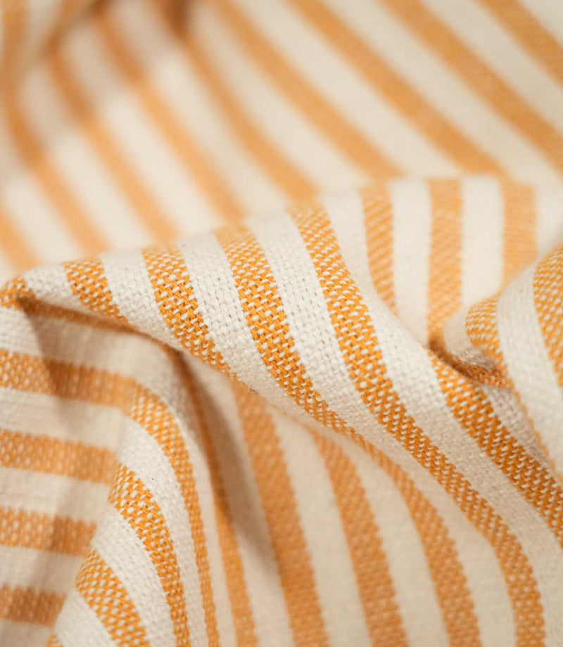 Macro close-up of draped Broadway Stripe Sunflower fabric, highlighting the individual woven threads, tactile surface and narrow sunflower orange stripes alternating with warm off-white stripes as the fabric forms soft folds.
