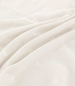 Close-up of Bumblebee Ivory fabric draped in soft folds, highlighting delicate white embroidered bees and the subtle texture of the ivory woven fabric.