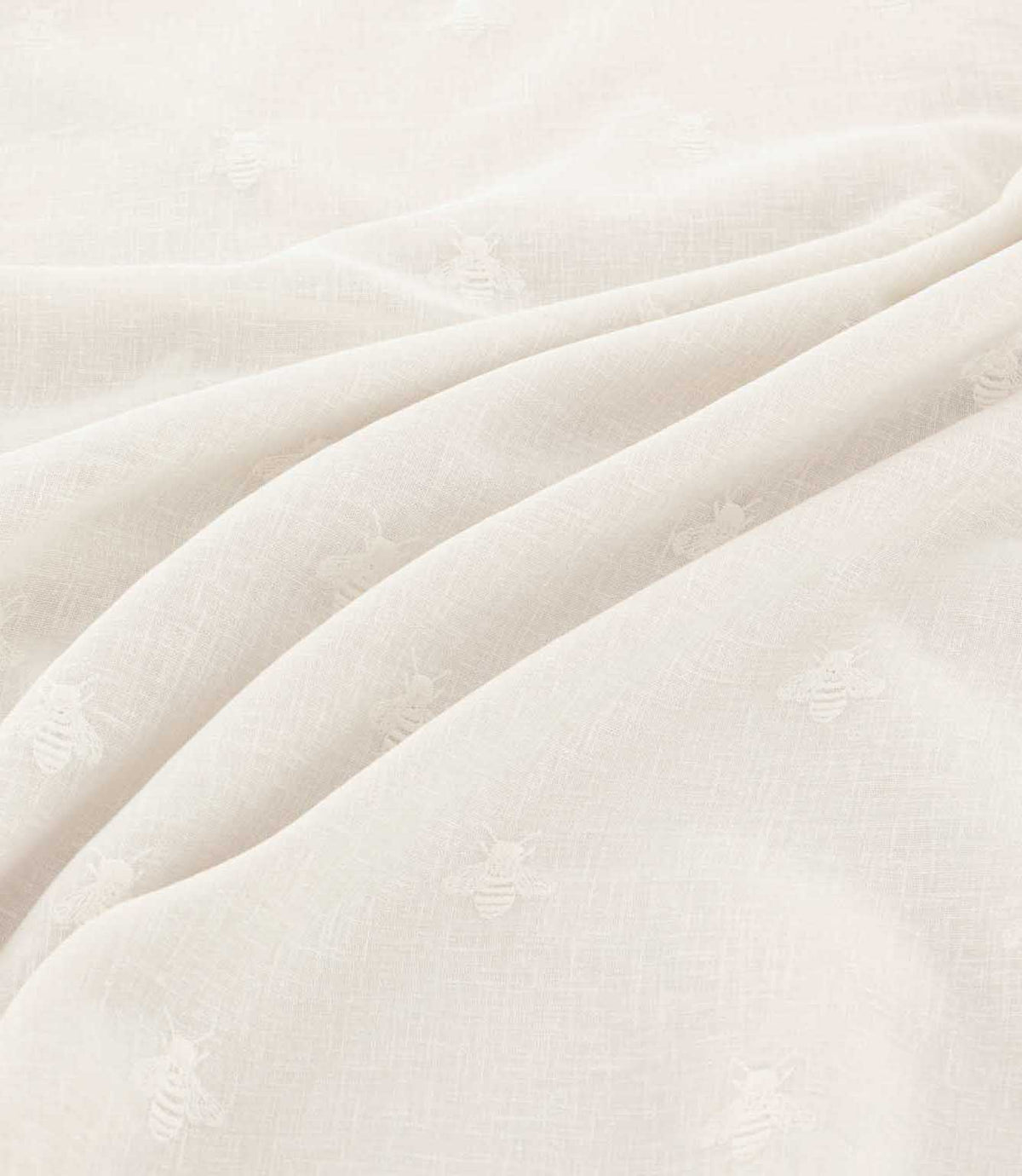 Close-up of Bumblebee Ivory fabric draped in soft folds, highlighting delicate white embroidered bees and the subtle texture of the ivory woven fabric.