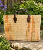 Woven basket tote bag with orange stripes and brown leather handles