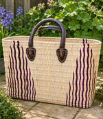 Woven basket tote bag with purple stripes and brown leather handles