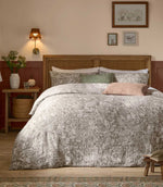 Voyage Maison Cademuir Reversible Muslin Duvet Cover Set in Nut, styled on a wooden bed with grey-brown woodland print bedding and coordinating cushions.