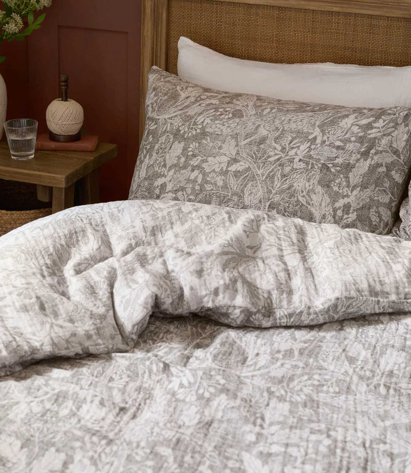 Close-up of Voyage Maison Cademuir duvet cover and pillowcase in Nut, showing the detailed grey-brown bird, foliage and woodland pattern.