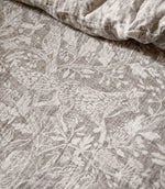 Close-up of Voyage Maison Cademuir bedding in Nut, showing the intricate grey-brown woodland print with birds, leaves, branches and botanical details.