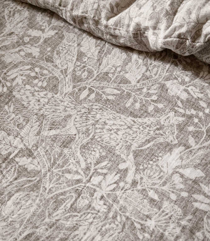 Close-up of Voyage Maison Cademuir bedding in Nut, showing the intricate grey-brown woodland print with birds, leaves, branches and botanical details.