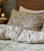 Close-up of Cademuir bedding by Voyage Maison in green and white, showing the detailed woodland pattern of birds, leaves and trailing foliage.