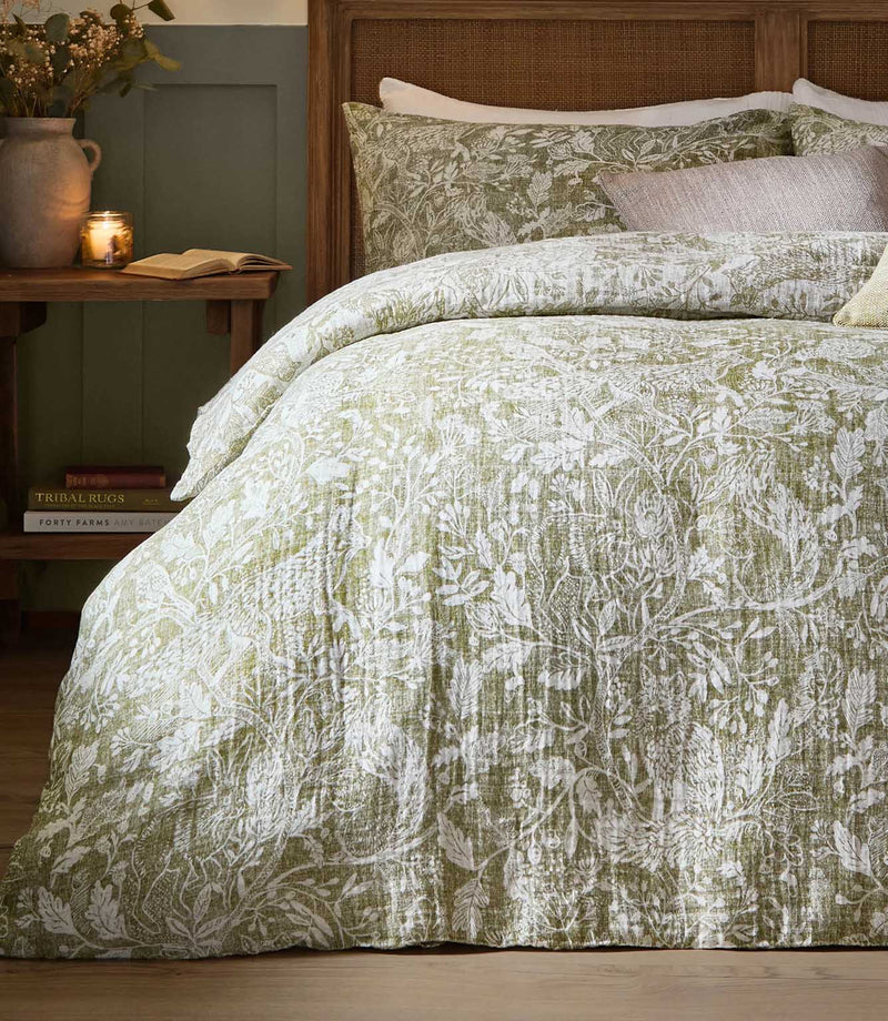 Voyage Maison Cademuir duvet cover set in green, featuring an intricate botanical and bird design with matching pillowcases on a wooden bed.