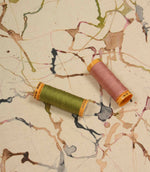 Carrara contemporary cotton linen fabric with coordinating thread spools highlighting the abstract print in green, pink, blue and neutral colours.