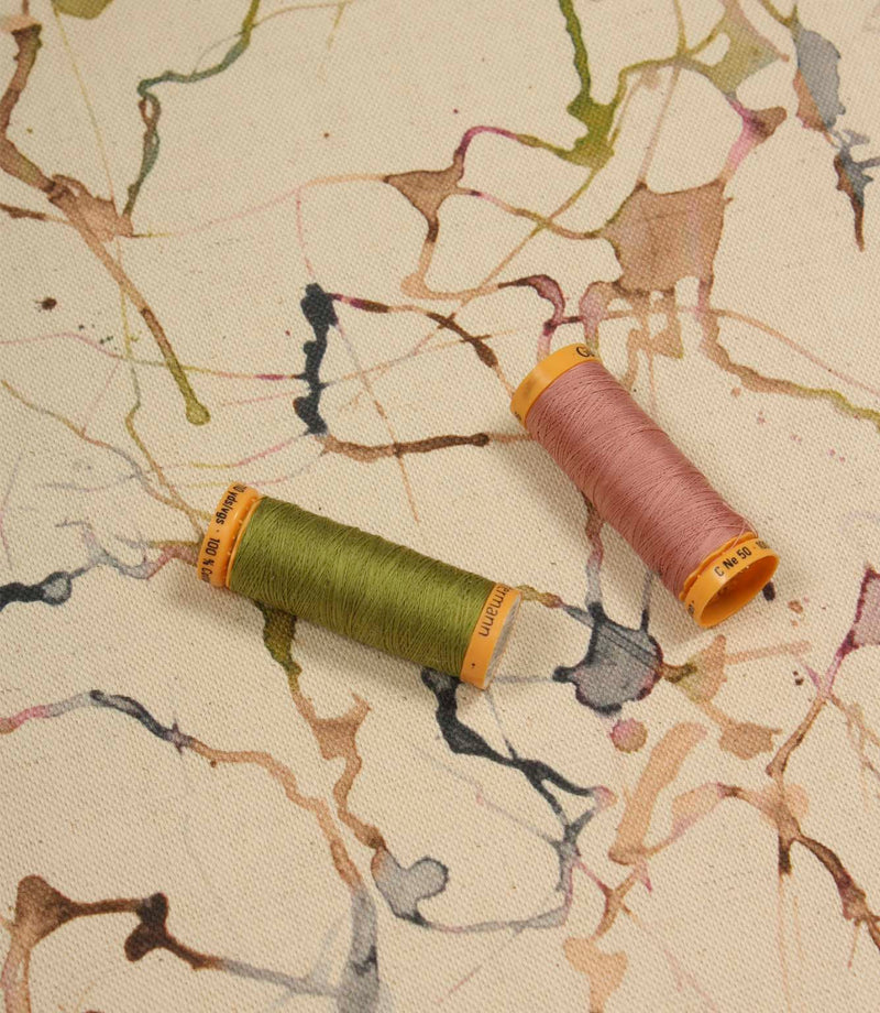 Carrara contemporary cotton linen fabric with coordinating thread spools highlighting the abstract print in green, pink, blue and neutral colours.