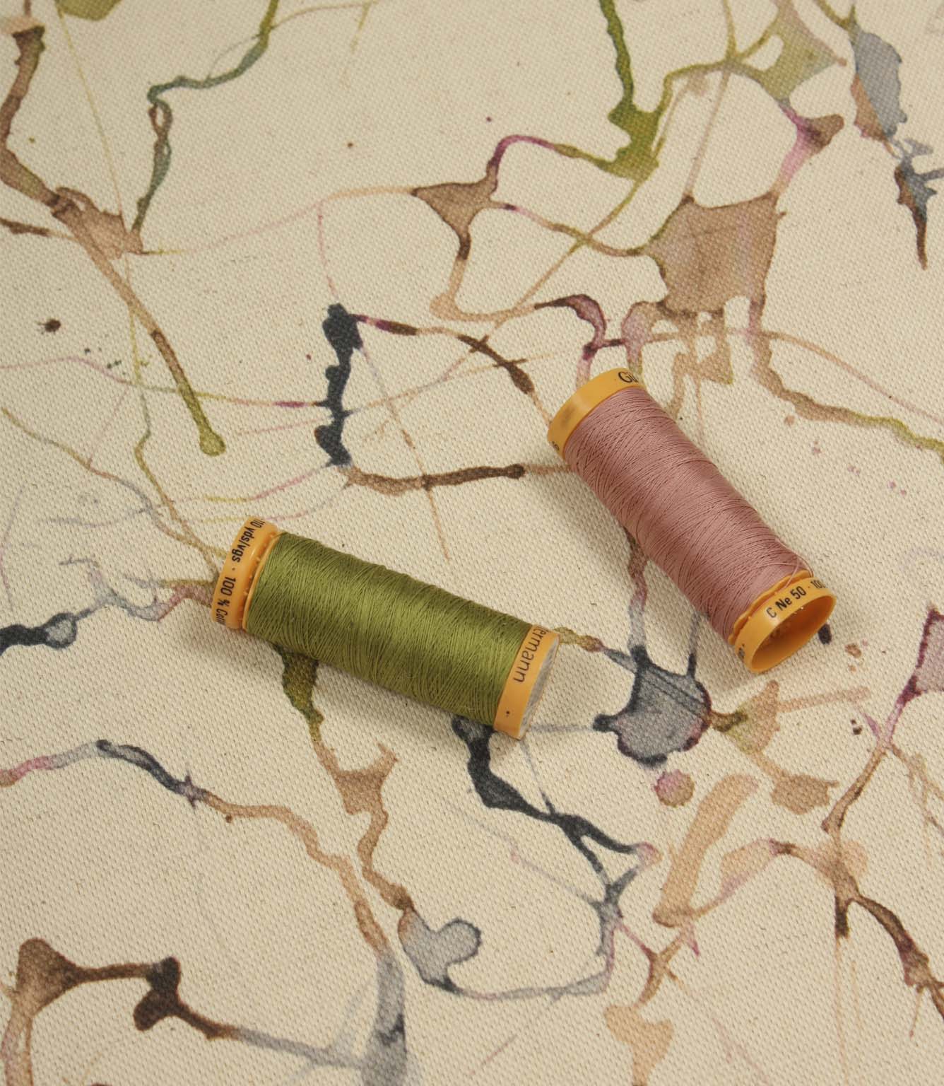 Carrara contemporary cotton linen fabric with coordinating thread spools highlighting the abstract print in green, pink, blue and neutral colours.