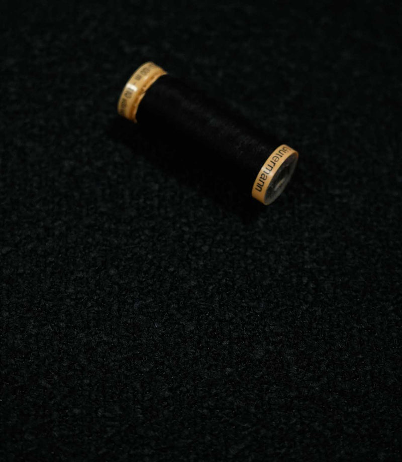 Case Bouclé Noir black fabric styled with a coordinating black thread spool, highlighting the textured bouclé weave and deep monochrome finish.